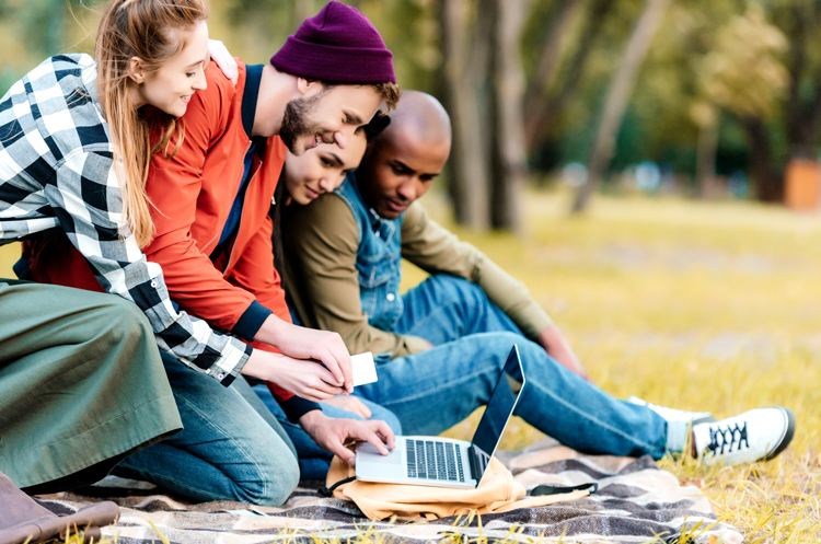 A group of young people in the park looking at a laptop