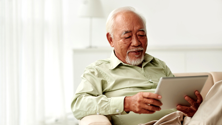 Elderly Man Sitting on Couch Looking at Tablet